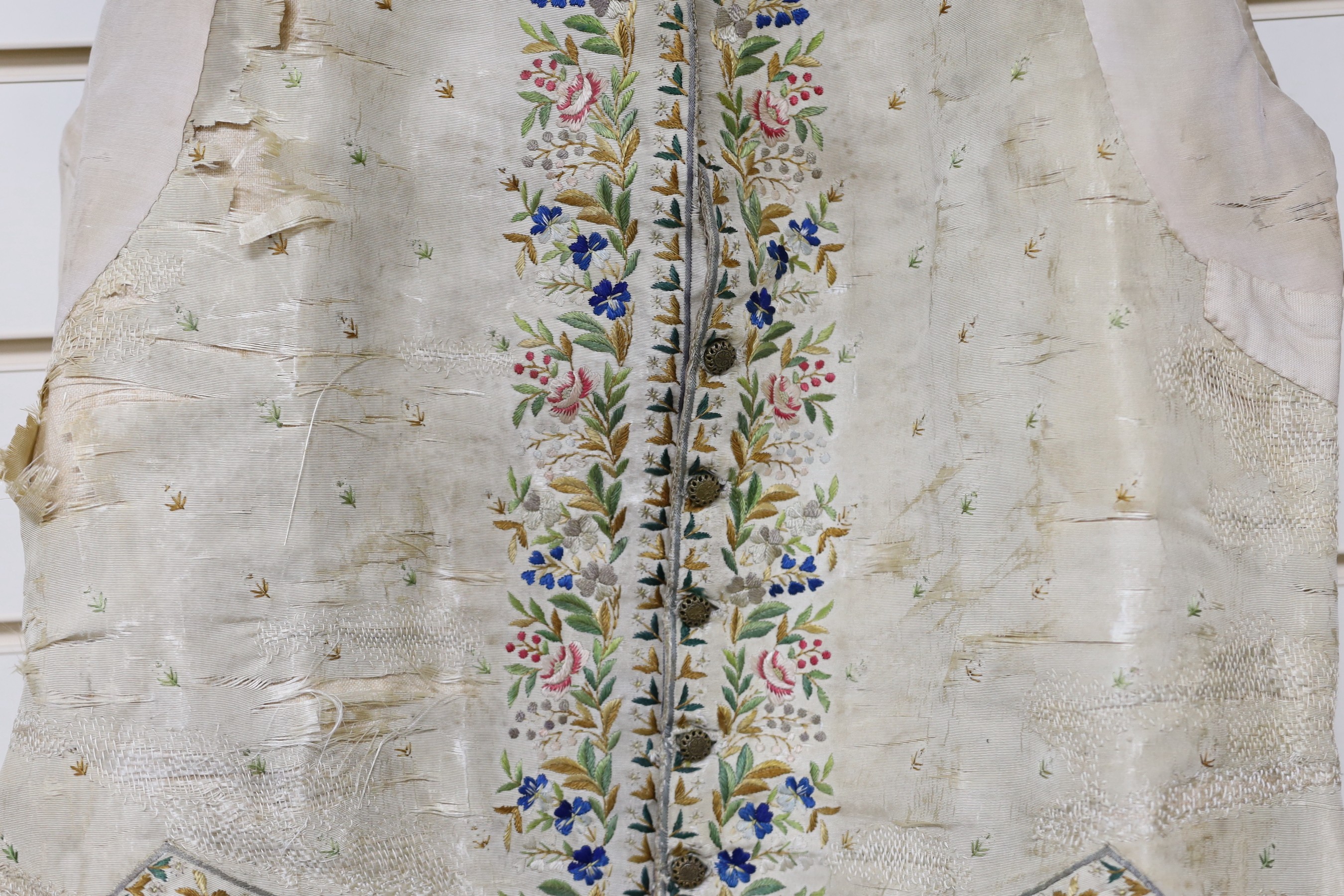 A late 18th early 19th century gentleman’s cream silk waistcoat Embroidered with polychrome silks in a floral design. (The main body of the waistcoat darned and damaged, but the embroidered sections complete).